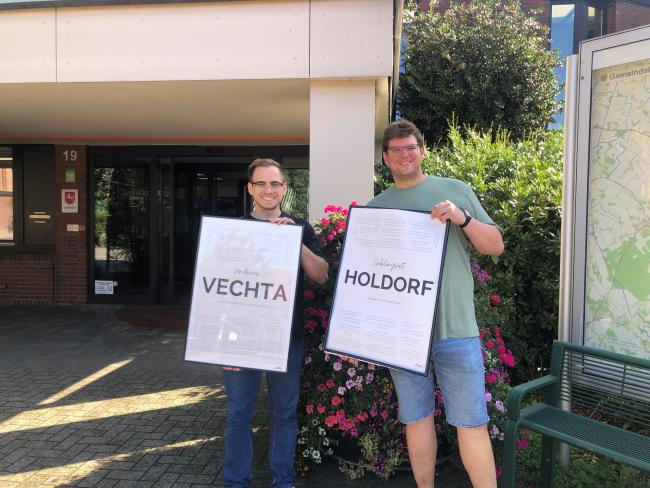 Der Jugendpfleger unseres Ortes, Timo Donner, zuständig für den Verein "Zukunft für Jugend e.V.", mit Praktikant Jakob Neveling (von der Uni Vechta), in den Händen haltend: einmal ein Plakat mit der Aufschrift "Lieblingsort Holdorf", einmal mit der Aufschrift "Lieblingsort Landkreis Vechta".